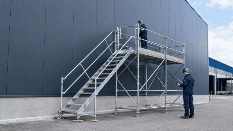 Arbeiten in der Höhe: Zwei Sicherheitskräfte auf Gerüst vor moderner Industriehalle.